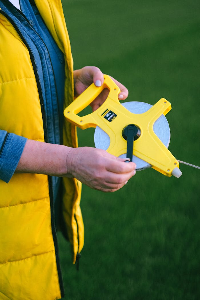 Close-up of hands holding a measuring tape outdoors on a grass field, ideal for agricultural themes.